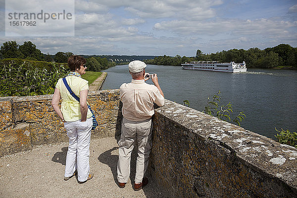 Ein Paar beobachtet die vorbeifahrenden Ausflugsboote auf der Seine von La Roche-Guyon  Frankreich.