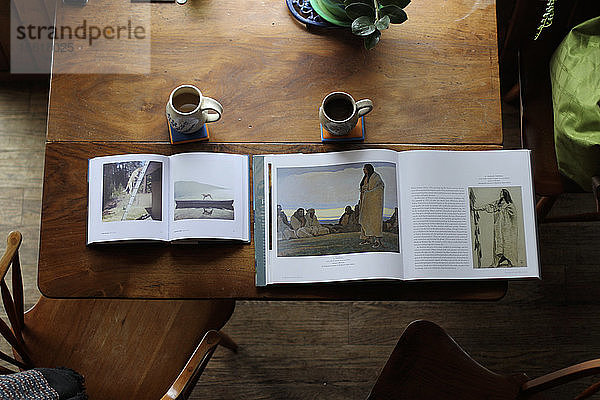 Zwei Bilderbücher und zwei Tassen Kaffee stehen morgens auf einem Holztisch