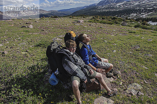 Die Jungen ruhen sich nach einem steilen Aufstieg zu einer hochalpinen Bank unterhalb des Kings Peak am vierten Tag der sechstägigen Rucksacktour von Troop 693 in der High Uintas Wilderness Area  Uintas Range  Utah  erschöpft auf einem Felsen aus.