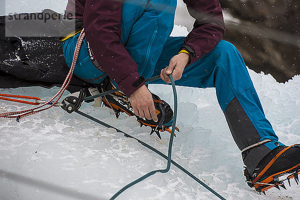 Bergsteigerin sitzt auf dem Eis und überprüft das Seil vor einem Eiskletterwettbewerb  Colorado  USA