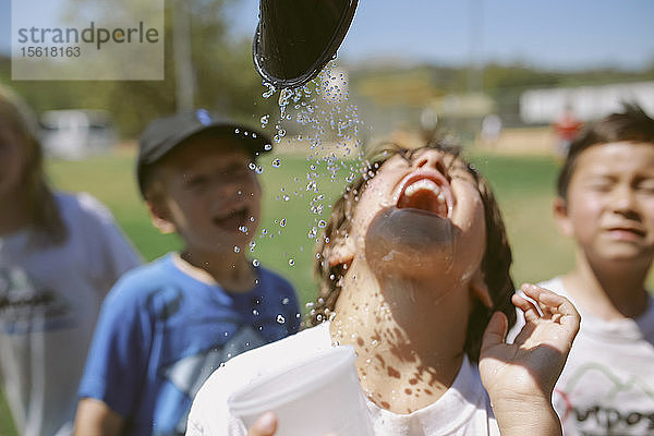 Eine Gruppe von Jungen kühlt sich in einer Spielpause mit einem Spritzer Wasser ab.
