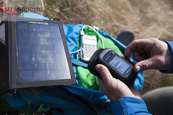 Ein Bergsteiger verwendet ein tragbares Solarpanel  um sein GPS während einer Klettertour aufzuladen