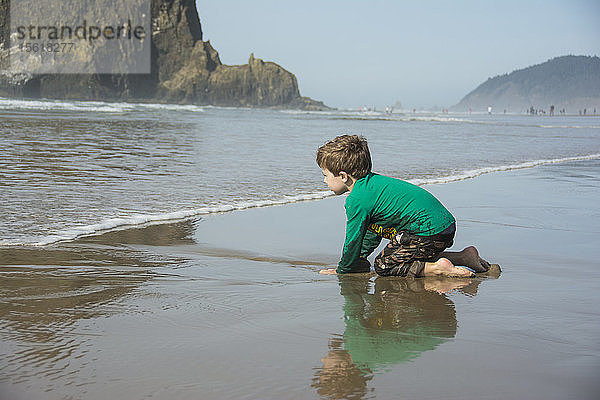 Ein kleiner Junge buddelt im Sand und freut sich auf die Wellen am Cannon Beach  Oregon.