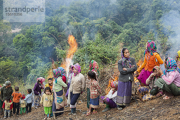 Frauen und Kinder stehen beiseite  während auf den Hügeln oberhalb von Muang Va  Laos  Feuer entzündet werden  wo die Dorfbewohner ihre Häuser vorübergehend umgesiedelt haben. Die bestehende Stadt wird durch den Nam-Ou-Damm Nr. 6 vollständig überflutet werden  und die von der Regierung vorgesehene Umsiedlung in der Nähe von Hat Sa wird nicht rechtzeitig abgeschlossen werden.