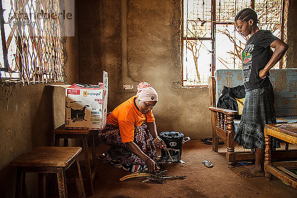 Die Solar Sister-Unternehmerin Fatma Mziray übergibt einen sauberen Holzkochherd an Zainabu Jabiri. Zainabu lernte Fatma einige Zeit zuvor kennen  als Fatma den Frauen in ihrem Dorf die sauberen Kochherde zeigte. Der Herd gefiel ihr und sie beschloss  sich einen anzuschaffen. Ihr gefiel die Idee  dass er viel weniger Brennholz verbraucht  kompakt ist und auch noch gut aussieht. Sie verkaufte Brennholz und Holzkohle  um Geld zu sparen und den Ofen kaufen zu können. Fatma spricht mit Zainabu und zeigt ihr dann  wie der Ofen funktioniert. In der Nähe von Arusha  Tansania. Fatma Mziray ist eine Solar Sister-Unternehmerin  die sowohl saubere Kochherde als auch Solarlaternen verkauft. Fatma hörte von einem Entwicklungshelfer von Solar Sister von den Kochern und beschloss  einen auszuprobieren. Der Rauch vom Kochen auf ihrem traditionellen Holzherd mit Brennholz verursachte ihr viele gesundheitliche Probleme  ihre Lungen waren verstopft  ihre Augen brannten und ihr Arzt sagte ihr  dass sie nicht mehr auf diese Weise kochen dürfe. An manchen Tagen fühlte sie sich so schlecht  dass sie nicht zum Kochen gehen konnte. Fatma sagte: ??????Um für eine Familie zu kochen  Frühstück  Mittag- und Abendessen zuzubereiten  musste ich früher jeden Tag eine große Ladung Holz sammeln. Jetzt  mit dem neuen Herd  reicht die gleiche Ladung Holz für bis zu drei Wochen Kochen. ??????Durch die zusätzliche Zeit kann ich mein Geschäft ausbauen. Außerdem habe ich mehr Zeit für meine Familie. Ich kann das Studium meiner Kinder ?????? überwachen. All das trägt zu einer glücklicheren Familie und einer besseren Beziehung zu meinem Mann bei. Seitdem ich den sauberen Herd benutze  ist niemand mehr krank geworden oder musste wegen einer Grippe ins Krankenhaus. ?????? Fatma sieht sich selbst als Helferin ihrer Gemeinschaft  denn sie sieht nicht mehr  dass die Menschen  denen sie Kochherde verkauft hat  rote Augen haben  husten oder krank sind  wie es früher der Fall war. Sie konnte das Schulgeld für ihre Kinder bezahlen  Dinge für den Haushalt und eine Kuh kaufen. ??????Ich stehe jeden Morgen früh auf  nehme meine Kocher und gehe in mein Geschäft  um meine Familie zur Schule zu bringen und Lebensmittel und andere Dinge für die Familie zu besorgen. ?????? Fatma hat es genossen  ein Teil von