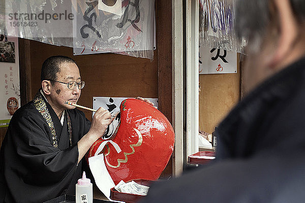 Ein Mönch malt ein Auge auf eine Daruma-Puppe