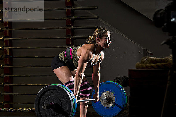 Ein Crossfit-Sportler trainiert mit schweren Gewichten an einer Langhantel in einem düsteren Fitnessstudio in San Diego  Kalifornien.
