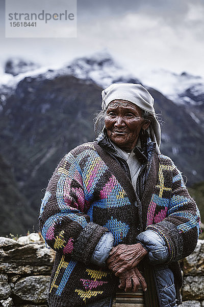 Eine ältere Sherpa-Frau in einem bunten Mantel steht vor den Bergen auf einer Kammlinie in der Nähe von Namche Bazaar  Solu Khumbu  Nepal