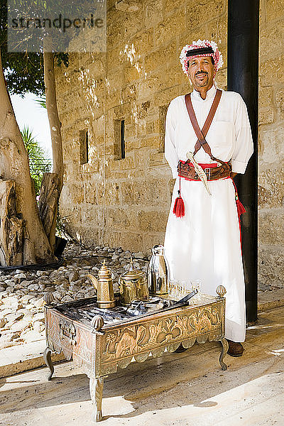 Porträt eines Mannes in traditioneller arabischer Kleidung  der vor einem traditionellen Teeservice auf einem gravierten Teetisch steht  Madaba Governorate  Jordanien