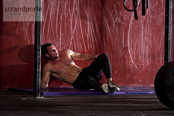 Ein Sportler sitzt nach einem intensiven Training in einem Fitnessstudio in San Diego  Kalifornien  mit Schmerzen auf dem Boden.