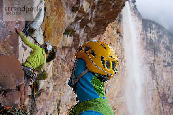 Mann mit Helm  der eine Person betrachtet  die auf den Felsen in der Nähe des Wasserfalls klettert  Bundesstaat Bolivar  Venezuela