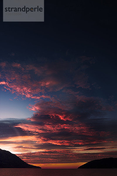 Sonnenaufgang über dem Adriatischen Meer im Januar. Rote Wolken  die vom Sonnenlicht beleuchtet werden  und die Insel auf der rechten Seite des Bildes. Aufgenommen in Budva  Montenegro.