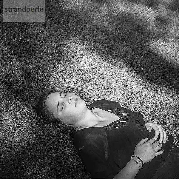 Eine junge Frau  die draußen auf einer Wiese im Schatten eines Baumes ein Nickerchen macht.