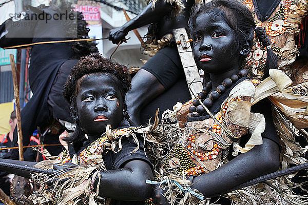 Kinder mit schwarz verschmierten Gesichtern in Stammeskostümen vor einem reitenden Mann beim Ati Atihan Festival  Kalibo  Aklan  Panay Island  Philippinen