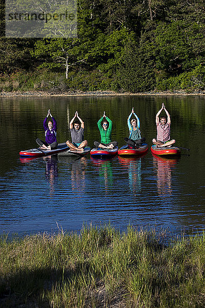 Foto mit einer Gruppe von fünf Personen  die Yoga auf einem Paddelbrett machen