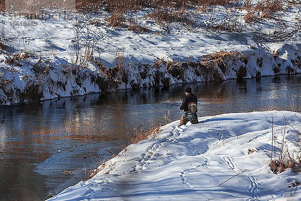 Ein Fliegenfischer steht knietief im Neuschnee  um seine Angel im Kickapoo River in Wisconsin's Driftless Region auszuwerfen.