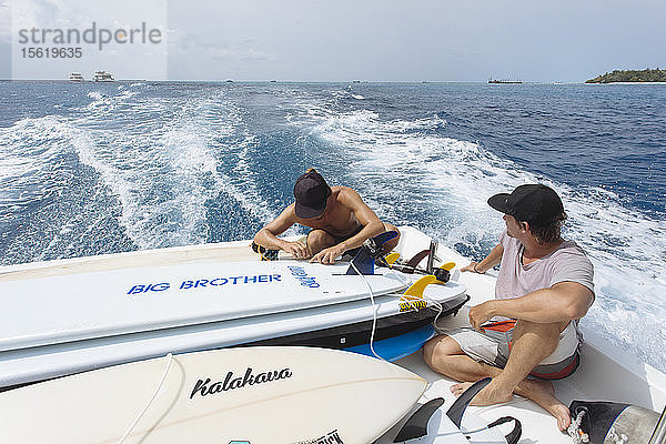 Zwei junge Männer sitzen auf einem fahrenden Motorboot  das Surfbretter transportiert  Male  Malediven