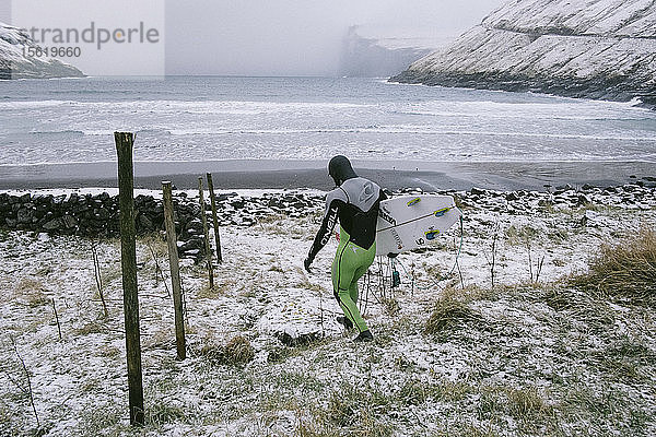 Profi-Surfer Indar Unanue auf dem Weg zum Wasser auf den Färöer Inseln. Er trägt einen dicken Neoprenanzug für die eiskalten Gewässer der subarktischen Bedingungen