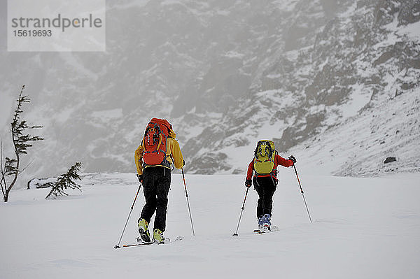 Bergsteiger nähern sich der Nordwand des Ptarmigan Peak (4.910 Fuß) auf Skiern während eines stürmischen Tages im Chugach State Park  in der Nähe von Anchorage  Alaska  Februar 2011. (Modellfreigabe: Agnes Hage  Kyle Irwin)