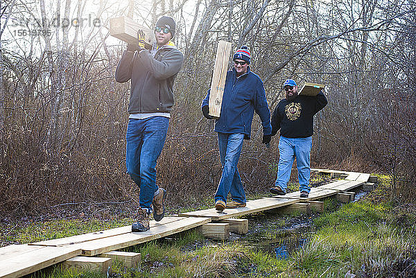 Freiwillige  die Bretter tragen  während sie gemeinsam einen Holzsteg als Teil eines Naturlehrpfads mit The Nature Conservancy bauen  Little Compton  Rhode Island  USA