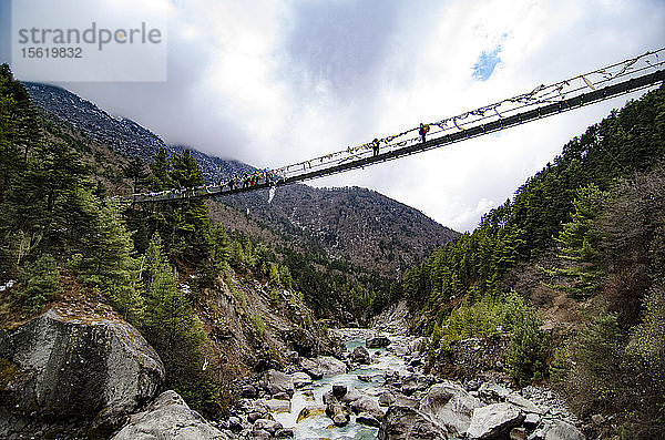 Wanderer überqueren eine Hängebrücke  die über Felsen und einen Bach führt  Solukhumbu  Nepal