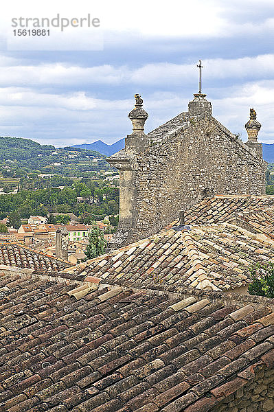 Ziegeldächer und eine Kirchenfassade umrahmen die provenzalische Landschaft von der Oberstadt Vaison-la-Romaine aus. Provence  Frankreich.
