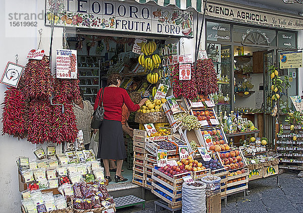 Frauen wählen Obst an einem Stand in einer Seitenstraße in Amalfi aus. Beachten Sie die Viagra Naturale (rote Chilischoten)  die für 5 Euro pro Strang verkauft werden. Amalfi ist eine Stadt und Gemeinde in der Provinz Salerno  in der Region Kampanien  Italien  am Golf von Salerno. Sie liegt an der Mündung einer tiefen Schlucht  am Fuße des Monte Cerreto (1.315 Meter)  umgeben von dramatischen Klippen und Küstenlandschaften. Die Stadt Amalfi war die Hauptstadt der Seerepublik Herzogtum Amalfi  einer wichtigen Handelsmacht im Mittelmeerraum zwischen 839 und etwa 1200. In den 1920er und 1930er Jahren war Amalfi ein beliebtes Urlaubsziel für die britische Oberschicht und Aristokratie. Amalfi ist der Hauptort der Küste  die Costiera Amalfitana (Amalfiküste) genannt wird  und ist heute zusammen mit anderen Orten an derselben Küste wie Positano  Ravello und anderen ein wichtiges Touristenziel. Amalfi ist Teil des UNESCO-Weltkulturerbes.
