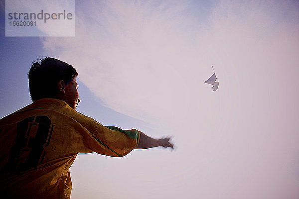 Rückansicht eines Jungen  der ein Papierflugzeug in den Himmel wirft
