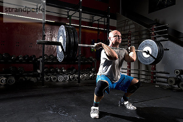 Ein athletischer Mann trainiert mit schweren Gewichten an einer Langhantel in einem düsteren Fitnessstudio in San Diego  Kalifornien.