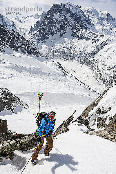 Bergführer  der sich mit den Skiern auf dem Rücken abseilt  um die Off-Piste zu erreichen