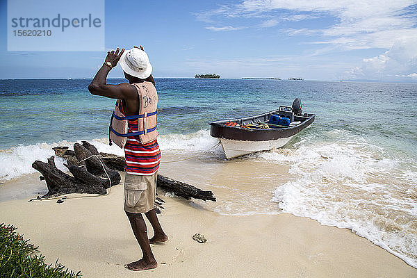 Ein Mann ergreift seinen Hut auf einer kleinen Insel der San-Blas-Inseln in Panama in der Karibik und blickt auf blaues Wasser und hellen Sand.
