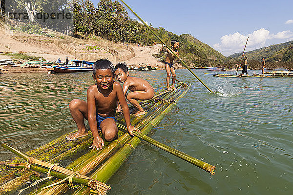 Kinder spielen im Nam Ou-Fluss auf Bambusflößen in Ban Hat Kham  Laos. Das Dorf würde durch den geplanten Staudamm Nr. 3 (mit dessen Bau noch nicht begonnen wurde) vollständig überflutet werden.