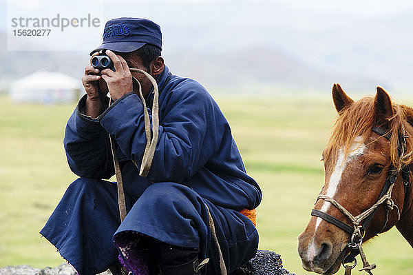 Ein mongolischer Bauer  der seine Pferdeherde mit einem Fernglas beobachtet  Mongolei