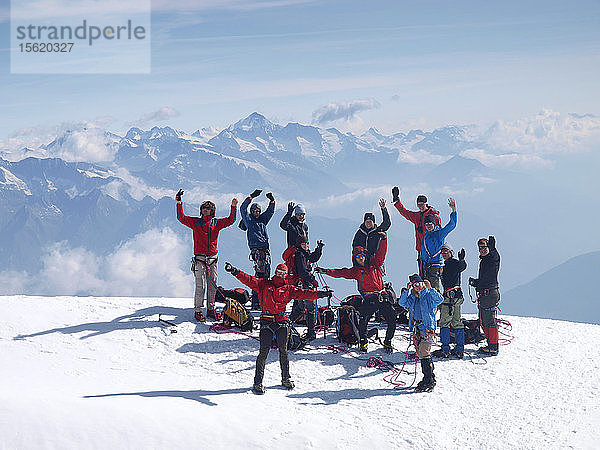 Eine Gruppe junger Leute steht winkend auf einem Berggipfel. Sie erreichten den Gipfel des Bishorns im Rahmen eines Junior-Bergsteigerkurses in den Schweizer Alpen.