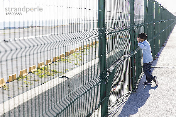 Ein kleiner Junge blickt durch den Zaun auf das Meer in Barcelona  Spanien