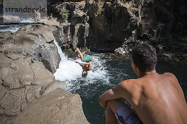 Junger Mann beim Klippenspringen in der Nähe eines Wasserfalls  ein anderer schaut zu  ï¾ McCloudï¾ River  Kalifornien  USA