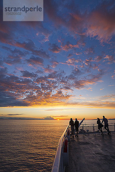 Silhouettierte Passagiere beobachten den Sonnenuntergang vom Oberdeck eines Fährschiffs in British Columbia