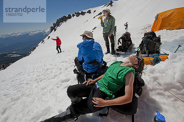 Jungen im Alter von 13 bis 17 Jahren von der Venturing Crew 191 aus Glendora  Kalifornien  setzen ein Jahr Training in die Praxis um  als sie versuchen  den Gipfel des Mount Shasta über die Avalanche Gulch-Route im Shasta Trinity National Forest in Nordkalifornien zu erreichen. Der Mount Shasta ist ein massiver  vergletscherter Vulkan und mit 14.179 Fuß der zweithöchste Gipfel in der Cascade Range und der fünfthöchste in Kalifornien; er ist mit keinem anderen Gipfel verbunden und erhebt sich abrupt 10.000 Fuß über das umliegende Gelände. Die Pfadfinder der Venturing Crew 191 (Venturing Crews sind ein Zweig der Pfadfinder  der sich auf abenteuerliche Aktivitäten konzentriert) hatten sich ein Jahr lang auf ihre Besteigung des Mount Shasta vorbereitet. Dies war ihre erste Erfahrung mit dem Klettern in steilem Schnee  und sie wurden bei ihrem Aufstieg von Führern der SWS Mountain Guides unterstützt. Die Jungen der Venturing Crew 191 (im Vordergrund - Tristan Rodriguez (grün) und Morgan Howlett (blau)) entspannen sich auf ihren Rucksäcken  nachdem sie in ihrem Hochlager auf etwa 10.000 Fuß auf dem Mount Shasta angekommen sind  während die SWS-Bergführer JB (rot) und Casey Hurden (grün) den Rest der Crew an den Hängen darunter suchen. Von diesem Lager aus wird die Crew vor der Morgendämmerung aufbrechen und versuchen  den Gipfel des Mount Shasta über die Avalanche Gulch Route zu erreichen  Shasta Trinity National Forest  Kalifornien