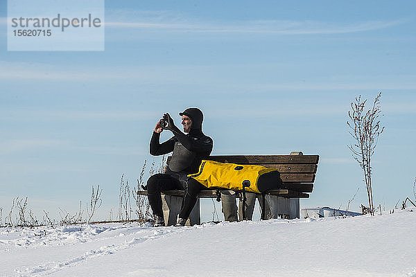 Ein Paddleboarder sitzt auf einer Bank in einem verschneiten Feld an der Küste von Maine