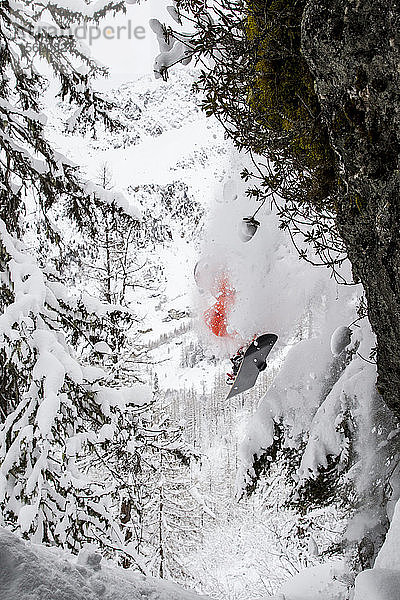 Ein Snowboarder springt von einer Klippe und lässt frischen Schnee fallen