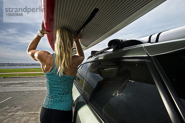 Ein Mädchen hebt ihr Paddelbrett vom Dach ihres Autos in San Diego  Kalifornien.