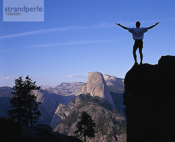 USA  Kalifornien  Yosemite-Nationalpark  Wanderer steht auf einem Felsblock mit Blick auf den Half Dome über dem Yosemite-Tal bei Sonnenuntergang