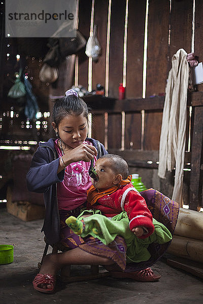 Ein Mädchen füttert ihren kleinen Bruder mit dem Löffel in ihrem Haus in Muang Hat Hin  Laos.