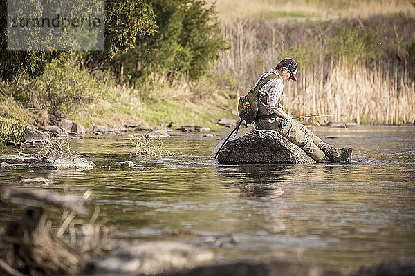 Eine Frau angelt mit der Fliege vom Ufer des Madison River in Montana.