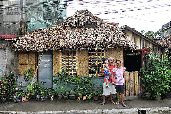 Porträt von Großeltern mit Kind  die vor einer Strohhütte in die Kamera schauen  Legazpi City  Provinz Albay  Philippinen