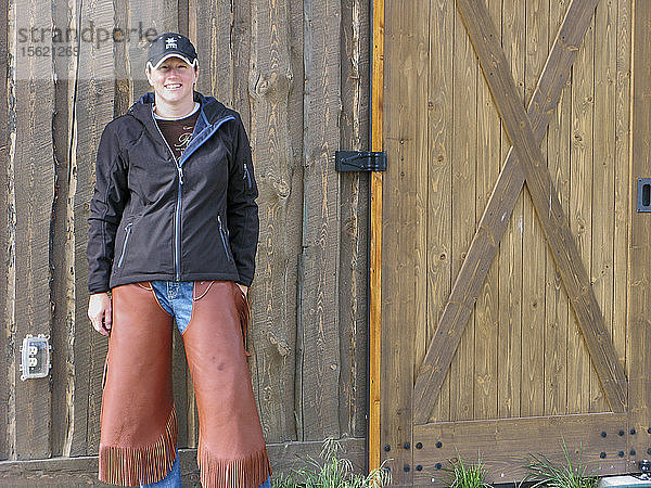 Vorderansicht einer lächelnden Frau in Chaps  die auf einen Ausritt auf einer Ranch wartet  Montana  USA