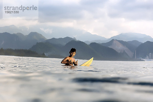 Junger Surfer zeigt Daumen hoch im Meer