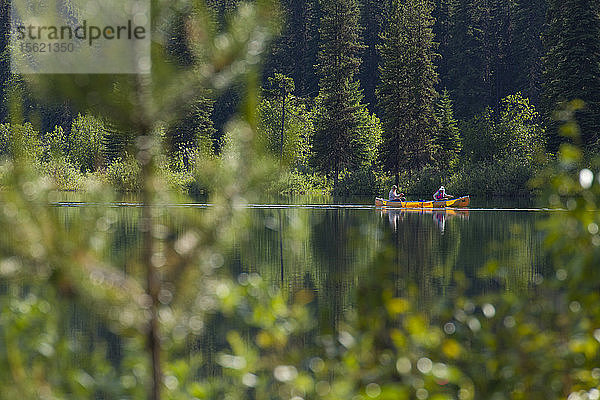 Ein Paar paddelt in einem gelben Kanu über den Unna Lake im Bowron Lake Provincial Park  British Columbia  Kanada.