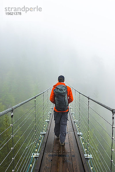 Ein Mann geht an einem regnerischen Herbsttag in Squamish  British Columbia  über eine Hängebrücke.