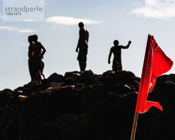 Silhouette einer Gruppe von jungen Männern  die auf einem Felsen im Waimea Bay Beach Park  O'ahu  Hawaii  USA  stehen